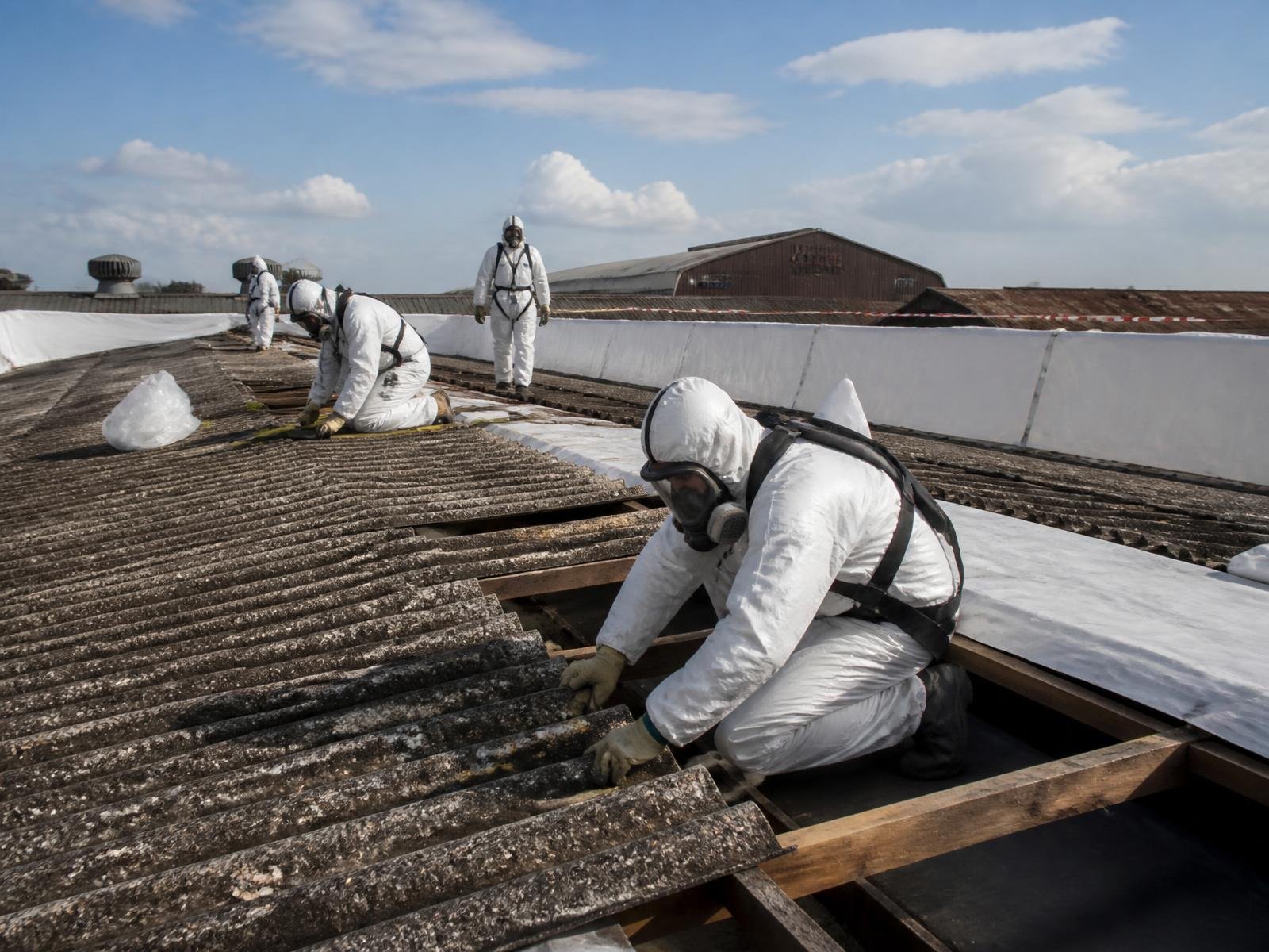 Workers in full PPE safely removing asbestos roofing sheets under containment